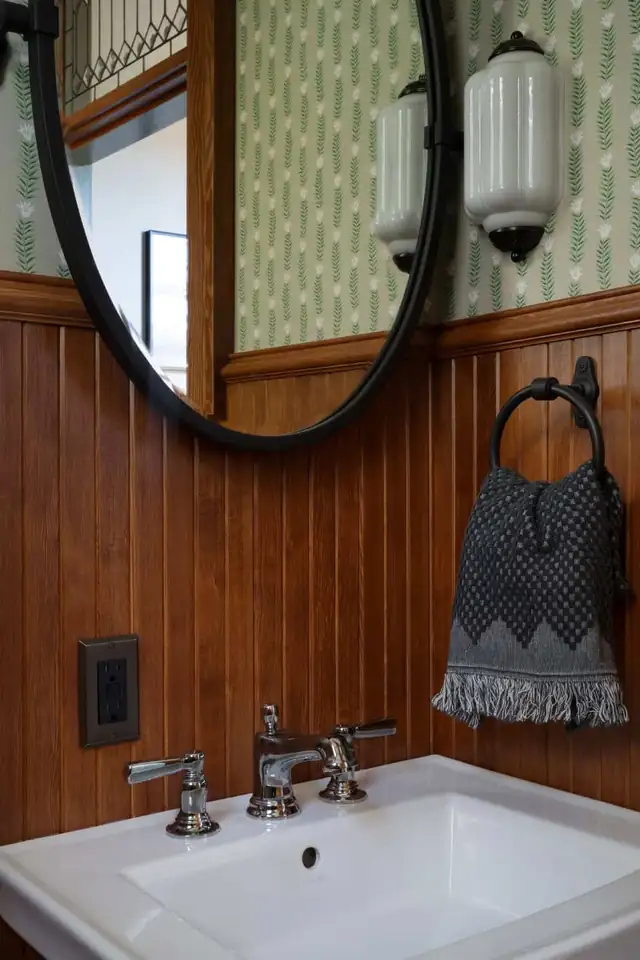 Powder bath with stained v-groove wood wainscot, patterned wallpaper, round mirror and wall-mount sink in NW Portland
