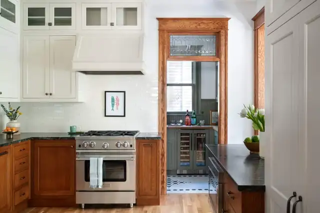 1902 NW Portland Craftsman kitchen with warm wood base cabinets, white glass-front uppers, range hood and leaded transom over the pantry door