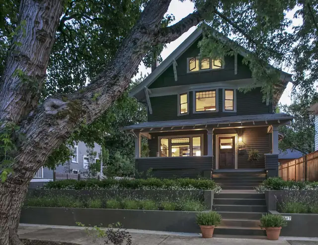 1910 Irvington Arts and Crafts house in Portland with dark green siding, deep eaves and lit front porch at dusk